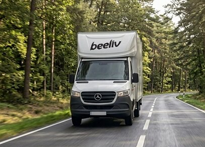 Camion de la marque Mercedes en cours de livraison visible sur une route en pleine forêt avec le logo BEELIV sur la capucine